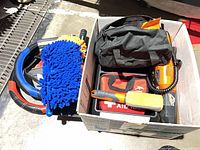 Overview of items in box including booster cables, chenille mitt, steering wheel covers, inflator, first aid kit, organizer tray