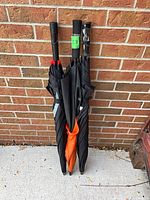Three folded black golf umbrellas leaning against brick wall