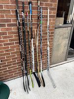 Eight hockey sticks leaning against wall showing shafts and blades