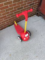Front side view of red Little Tikes 3-wheel push scooter showing handlebar, wheels and face graphic