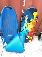 Front view of blue plastic sled, top of foam slide board with graphic, rolled blue mat visible