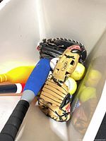 Bin with tan Rawlings glove, blue foam bat and yellow softballs