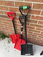 Three snow shovels leaning against brick wall, front view