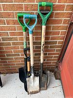 All four shovels leaning against brick wall, full length view