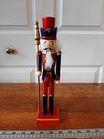 Front view of wooden nutcracker soldier holding spear on red base beside ruler