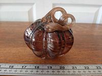 Front view of purple and gold art glass pumpkin beside ruler