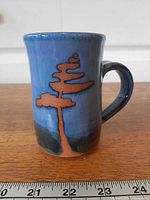 Front view of blue ceramic mug showing tree motif and ruler for scale