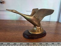 left profile of brass goose on wood base with ruler for scale