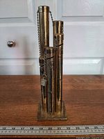 Front view of brass coin sorter showing four tubes, graduations, padlock, and base with ruler for scale