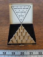 brass triangular board with pegs inserted inside hinged box, instruction panel visible