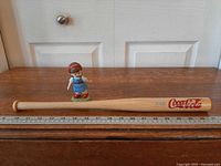 Hamilton figurine beside wooden mini bat placed on ruler