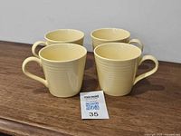 Four yellow ribbed mugs grouped on wooden surface