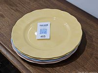Stack of five pastel plates showing top yellow plate and MaxSold ID card