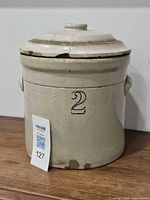 Front view of beige stoneware crock marked 2 with lid, showing side handle and rim crack