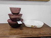 Stacked three cranberry mixing bowls with lids and English Pyrex casserole