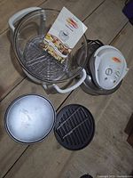 Complete FlavorWave Turbo oven set laid out: heating lid, glass bowl on base, wire rack, grill pan, metal lid, manual