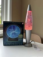 Front view of boxed Lumindisk next to illuminated glitter lamp