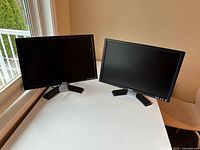 Both Dell monitors on tabletop, screens off