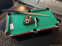 Full view of tabletop pool table with cues, balls in rack, and brush on playing surface