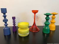 Front view of six multicolor candle holders on black surface