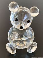 Front view of clear faceted crystal bear figurine showing tilted head, round ears, black eyes and nose