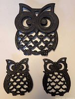 Front view of three cast iron owl trivets, large at top, two smaller below
