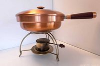 Side view of assembled copper-finish chafing dish on brass-tone stand with burner