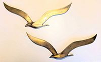 Two brass seagull wall hangings displayed on wall