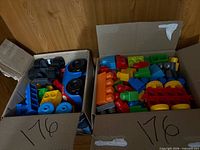 Two open cardboard boxes showing quantity and variety of oversize plastic interlocking blocks, wheels and car base