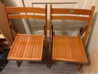 Two wooden folding chairs unfolded, showing seats and backs