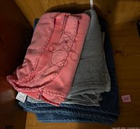Stack of three folded blankets: pink on top, grey in middle, blue at bottom
