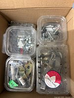 Close-up of open cardboard box showing five clamshell containers of assorted hardware