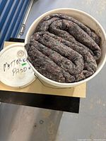 Top view of white bucket filled with coiled grey multicoloured felt padding; lid labeled