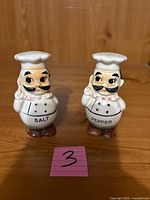 Front view of both ceramic chef shakers showing labels and painted details