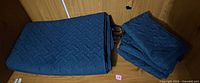 Folded dark blue quilted blanket and stacked matching pillow covers