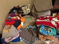 Pile of assorted children’s garments including graphic T-shirts, knit hat, camouflage items
