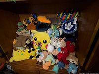 Group of plush toys including Pikachu pillow, Toronto Maple Leafs pillow, Baby Yoda, Michelangelo and others
