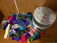 Pile of multicolour knitted warmers beside round bird-print decor box with lid