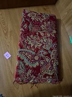 Folded red tapestry-pattern fabric remnant showing floral and paisley design with frayed edges
