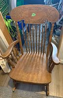 Front view of wooden rocking chair showing carved crest rail, turned spindles, arms, seat and rocker runners