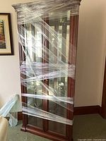 Full view of wood and glass corner cabinet wrapped for transport