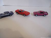 Three die-cast cars lined up: blue, red, pink