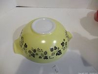 Exterior side view of yellow Pyrex bowl showing black fruit pattern and spouts