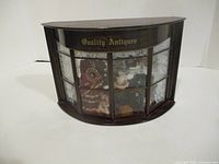Front view of curved wooden shadow box labelled Quality Antiques
