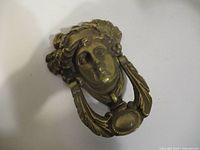 Front view of brass door knocker showing female face and striker