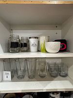 Shelf showing entire assortment: mason jar mugs, travel tumblers, bowl, mug, tall and short glasses
