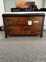 Front view of rustic brown storage bench with black cushioned seat