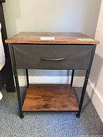 Front view of bedside table showing fabric drawer, wood-look top, metal frame, lower shelf