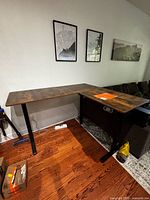 Overall view of L-shaped desk against wall, showing brown top and black legs