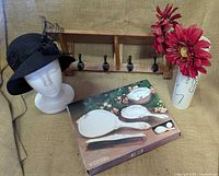 Overall lot showing vanity set box, hat on mannequin head, wood shelf with hooks, wood vase with flowers, ceramic vase